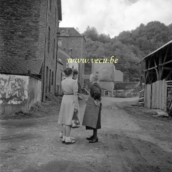 photo ancienne  Deux citadines en conversation avec une femme du village. La maison à l'arrière plan est une boulangerie-patisserie